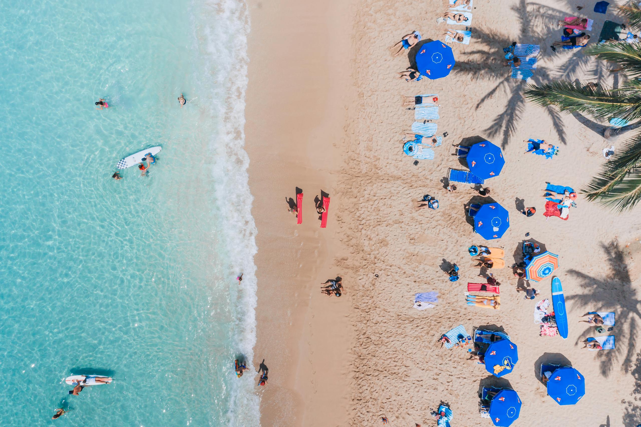 An aerial view capturing a lively beach scene in Hawaii with surfers and beachgoers.