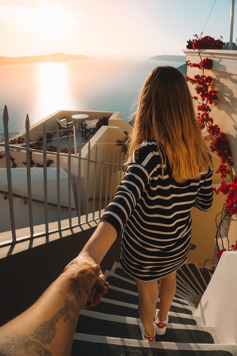 Couple holding hands descending stairs with a stunning Santorini sunset view.